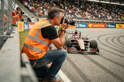 Photographe de presse accroupi en bord de piste lors d'une course automobile, grandstands bondés en arrière-plan